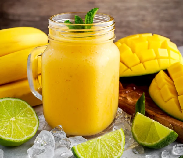 Gezonde rijpe gele banaan Mango Smoothie met plakjes van kalk, mint en ijs — Stockfoto