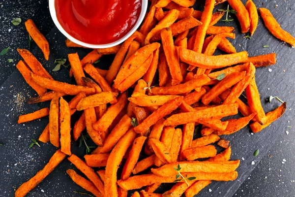 Patatas fritas dulces de naranja horneadas caseras saludables con salsa de tomate, hierbas, sal y pimienta . — Foto de Stock