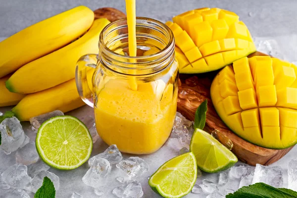 Batido de mango de plátano amarillo maduro saludable con rodajas de lima, menta y hielo — Foto de Stock