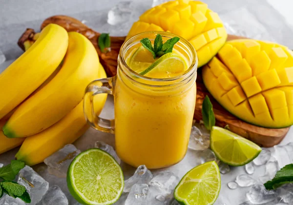 Batido de mango de plátano amarillo maduro saludable con rodajas de lima, menta y hielo —  Fotos de Stock