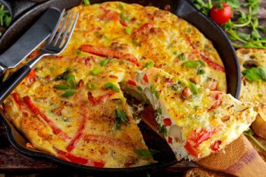 Yumurta, patates, pastırma, kırmızı biber, maydanoz, yeşil bezelye, soğan, demir tavada peynir Frittata yapılmış. ahşap masa.