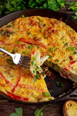 Yumurta, patates, pastırma, kırmızı biber, maydanoz, yeşil bezelye, soğan, demir tavada peynir Frittata yapılmış. ahşap masa.