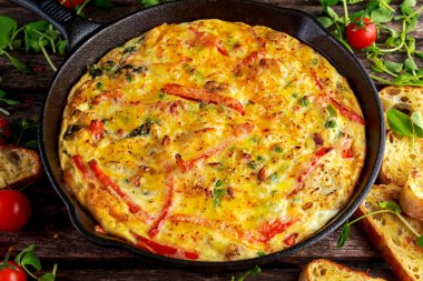 Yumurta, patates, pastırma, kırmızı biber, maydanoz, yeşil bezelye, soğan, demir tavada peynir Frittata yapılmış. ahşap masa.