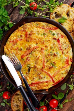 Yumurta, patates, pastırma, kırmızı biber, maydanoz, yeşil bezelye, soğan, demir tavada peynir Frittata yapılmış. ahşap masa.