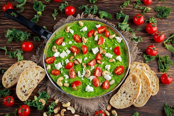 Verdure Omelette verde con pomodori, cavolo riccio, formaggio greco, olive, noci, pane tostato su fondo di legno. concetto cibo sano — Foto Stock