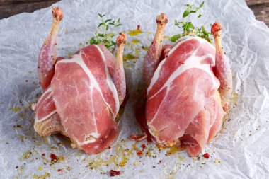 Ready to cook raw seasoned partridges with bacon on crumpled paper. clipart