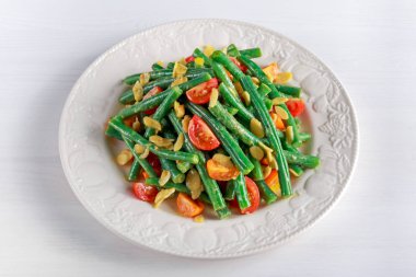 Kırmızı, sarı domates, bruschettas ve beyaz tabakta kuşbaşı badem yeşil fasulye salatası