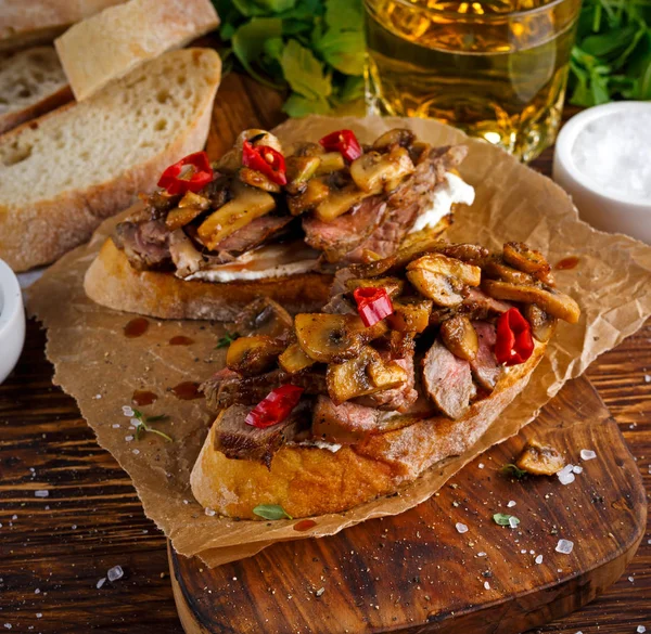 Sanduíche de Bife Grelhado com cogumelos, manteiga de queijo de cabra e folhas de rúcula em cima. cerveja dourada . — Fotografia de Stock