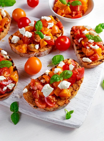 Läckra traditionella tomat bruschetta med fetaost toppning, färsk basilika. — Stockfoto