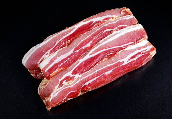 Raw smoked streaky sliced bacon on black board background