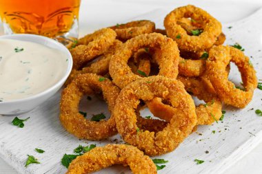 Fried kotletpane soğan halkaları sos ve Beyaz ahşap tahta, arka plan ışığı bira ile