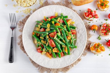 Green beans salad with Red, Yellow Tomatoes, bruschettas and flaked almond on white plate clipart