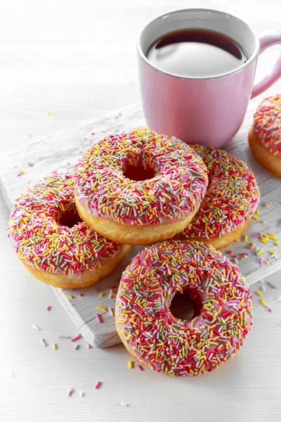 Iced doughnut rings with rainbow sparkl strands and cup of coffee, tea — Stock Photo, Image