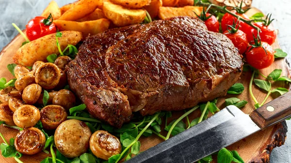 Vařené hovězí Ribeye Steak s brambory, houby, rajčata na dřevěné desce. — Stock fotografie