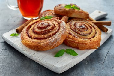 Taze pişmiş geleneksel tatlı tarçın rulo, girdap sıcak siyah çay ve nane ile beyaz ahşap tahta üzerinde