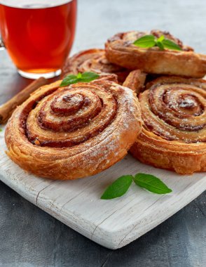 Taze pişmiş geleneksel tatlı tarçın rulo, girdap sıcak siyah çay ve nane ile beyaz ahşap tahta üzerinde
