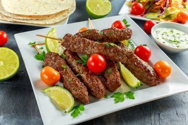 Ev yapımı köfte kebap pide, kireç, sebze, tatlı biber ve yoğurt sos beyaz plaka üzerinde şiş üzerinde.