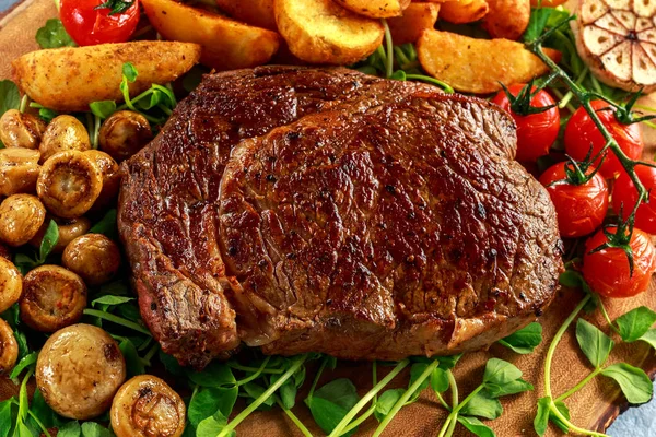 Vařené hovězí Ribeye Steak s brambory, houby, rajčata na dřevěné desce. — Stock fotografie