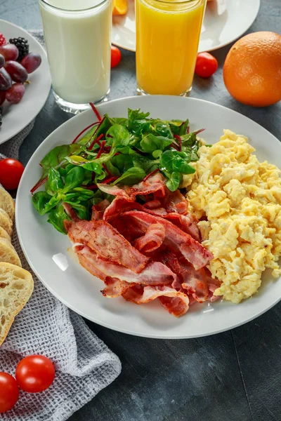 Manhã Ovo mexido, bacon café da manhã com suco de laranja, leite, frutas, pão no prato branco — Fotografia de Stock