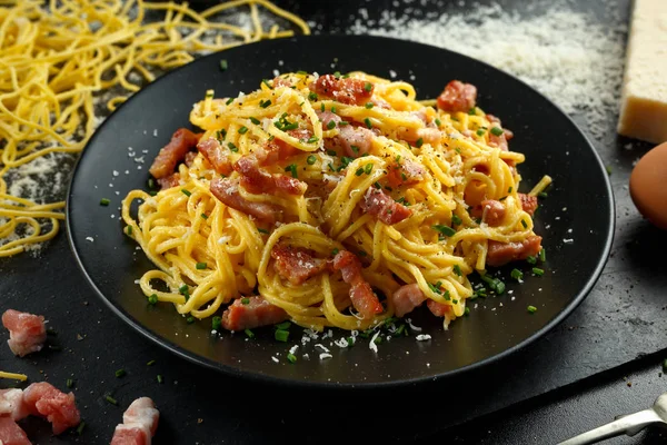 Klasyczny domowy makaron carbonara włoski z boczkiem, jajka, ser parmezan na czarnej płycie. — Zdjęcie stockowe