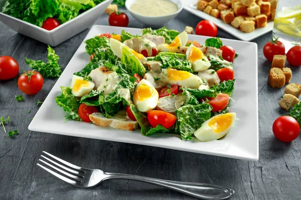 Свежий здоровый салат Цезарь с курицей, яйцами, помидорами, сыром и гренками на белой тарелке — стоковое фото