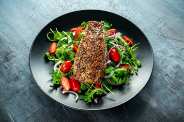 Domates, füme uskumru salatası doğranmış kırmızı soğan, Ruccola siyah plaka üzerinde.