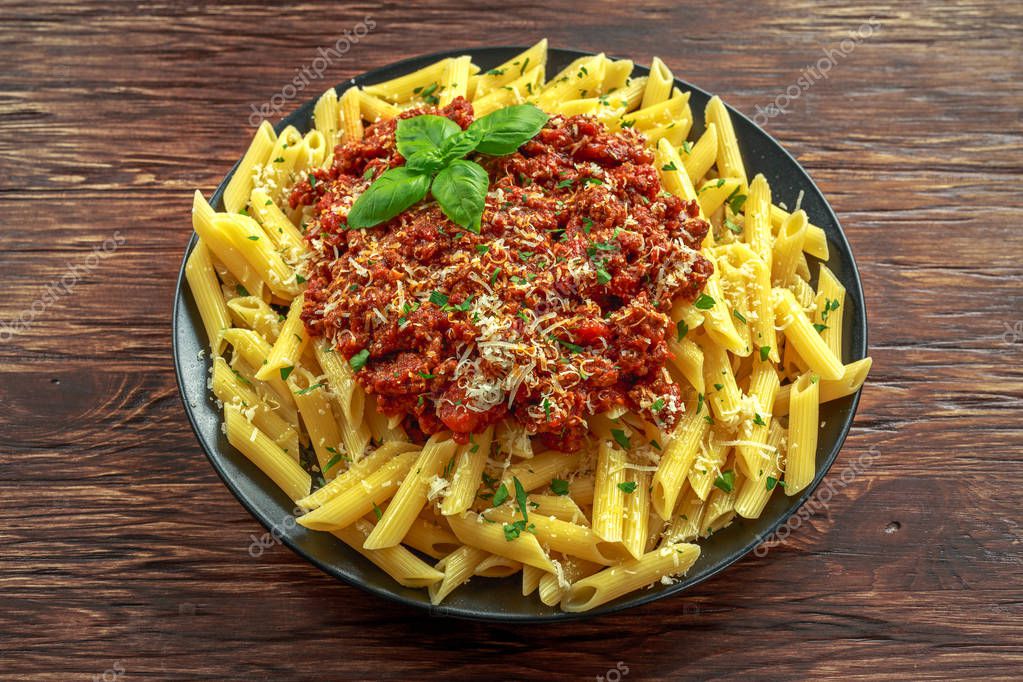 Hot Penne pasta bolognese with parmesan cheese, basil on top. on wooden