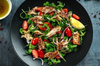 Domates, füme uskumru salatası doğranmış kırmızı soğan, Ruccola siyah plaka üzerinde.