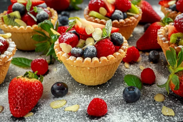 Tartaletas de bayas con arándanos, frambuesas, kiwi, fresas, hojuelas de almendras en azúcar glas . — Foto de Stock