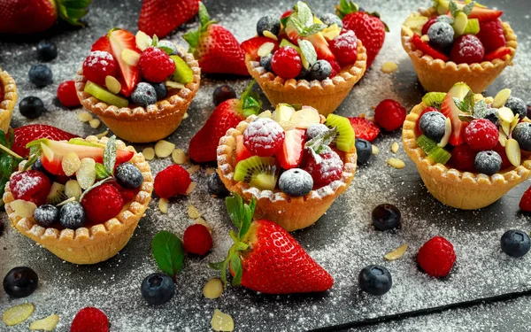Tartelettes aux baies aux myrtilles, framboises, kiwis, fraises, flocons d'amandes dans du sucre glace . — Photo