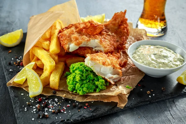 Brittiska traditionella fisk och chips med mosade ärtor, tartarsås på skrynkligt papper med kall öl. — Stockfoto