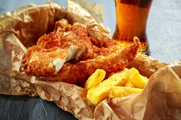 British Traditional Fish and chips in crumpled paper with cold beer.