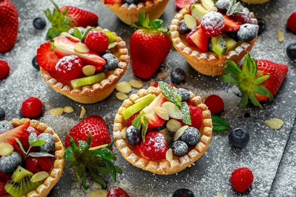 Tartaletas de bayas con arándanos, frambuesas, kiwi, fresas, hojuelas de almendras en azúcar glas . — Foto de Stock
