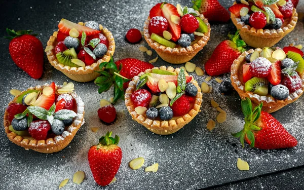 Berry tartlets med blåbär, hallon, kiwi, jordgubbar, mandel flingor i florsocker. — Stockfoto