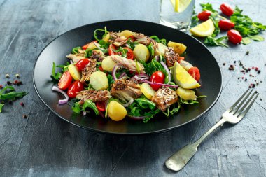 Yeni patates, domates, doğranmış kırmızı soğan ve Ruccola siyah plaka üzerine haşlanmış sıcak füme uskumru salatası.