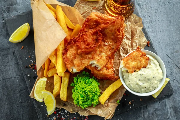 British Traditional Fish and chips with mashed peas, tartar sauce on crumpled paper with cold beer.