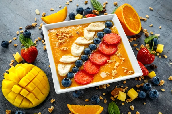 Batido de naranja fresca en tazón para el desayuno con arándanos, granola, mango, fresa y plátano —  Fotos de Stock