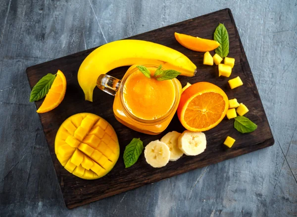 Muz, mango, havuç siyah ahşap tahta üzerinde taze Portakallı gazoz içmek. — Stok fotoğraf