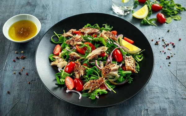 Domates, füme uskumru salatası doğranmış kırmızı soğan, Ruccola siyah plaka üzerinde.