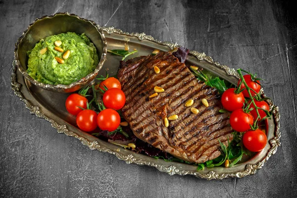 Grilled Ribeye steak served on salad pillow with pesto, pine nuts and cherry tomatoes on a vitage plate