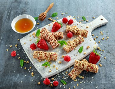 Çilek, ahududu tatlım ve beyaz kesme tahtası üzerinde çikolata granola bar