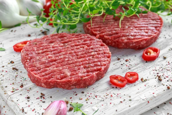 Fresh raw beef, round patties for making homemade burger on wooden white board