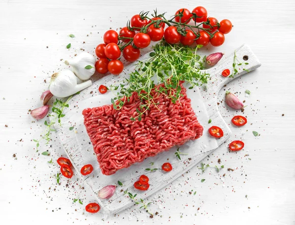 Carne picada fresca de res cruda con sal, pimienta, chile y tomillo fresco en pizarra blanca . — Foto de Stock