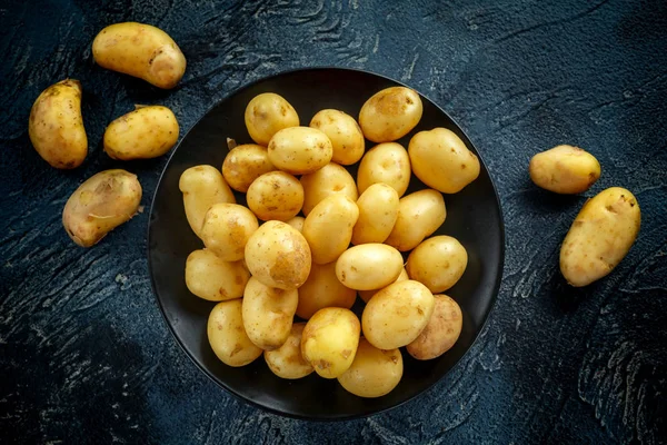 Bebê cru batatas novas em placa preta — Fotografia de Stock