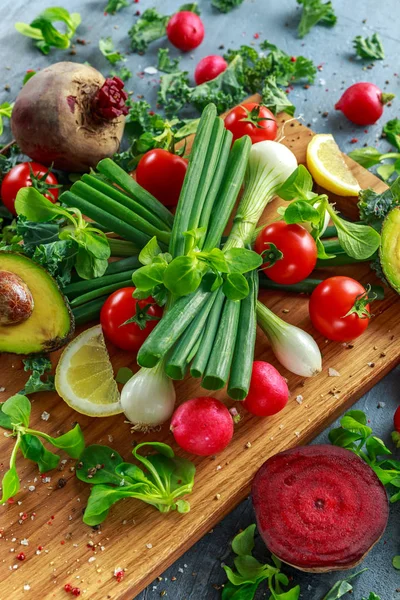 Seasonal vegetables ingredient for salad, red radish, tomatoes, spring onions, beetroot, lemons and avocado on oak cutting board with sea salt and corn peppers — Stock Photo, Image