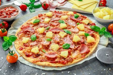 Taze pişmiş pizza hawaii ile jambon ve ananas, fesleğen, domates yedeklenmiş kağıt üzerinde
