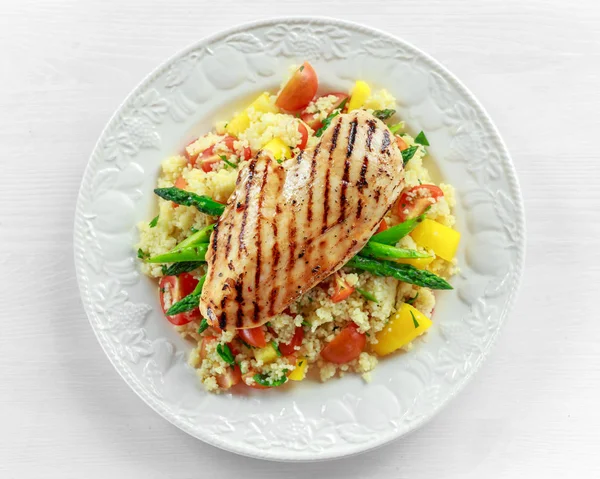 couscous salad with grilled chicken and asparagus on white plate. wooden table. healthy food