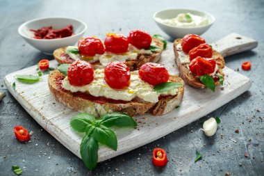 Domates Ricotta Bruschetta güneş ile kurutulmuş domates Yapıştır, zeytinyağı kahverengi ekmek ve Beyaz ahşap tahta fesleğen.