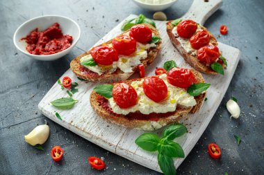 Domates Ricotta Bruschetta güneş ile kurutulmuş domates Yapıştır, zeytinyağı kahverengi ekmek ve Beyaz ahşap tahta fesleğen.