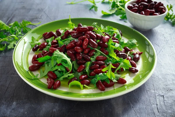 Haricots rouges et salade santé roquette sauvage dans une assiette verte — Photo